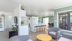 A modern living room with grey sofas, a wooden coffee table, and a kitchen area with a bar stool set.