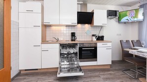 Een praktische keuken met witte kastjes, een vaatwasser, een oven, een magnetron en een televisie aan de muur.