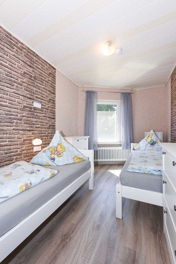 A room with two single beds, a brick wall, a window with curtains, and a radiator. - Apartment "South" - Ferienhof "Tannen" (Stedesdorf)