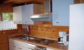 Cozinha compacta com paredes de madeira, pia de aço inoxidável, fogão e cafeteira.