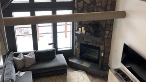 A modern living room with a stone fireplace, a large window, a sofa, and a TV. - Renovated  Running Y Ranch Resort Home (Klamath Falls)