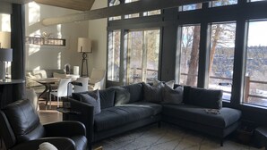 A modern living room with a sectional sofa, a white armchair, and a dining area with a table and chairs. Large windows provide a view of the outdoors. - Renovated  Running Y Ranch Resort Home (Klamath Falls)