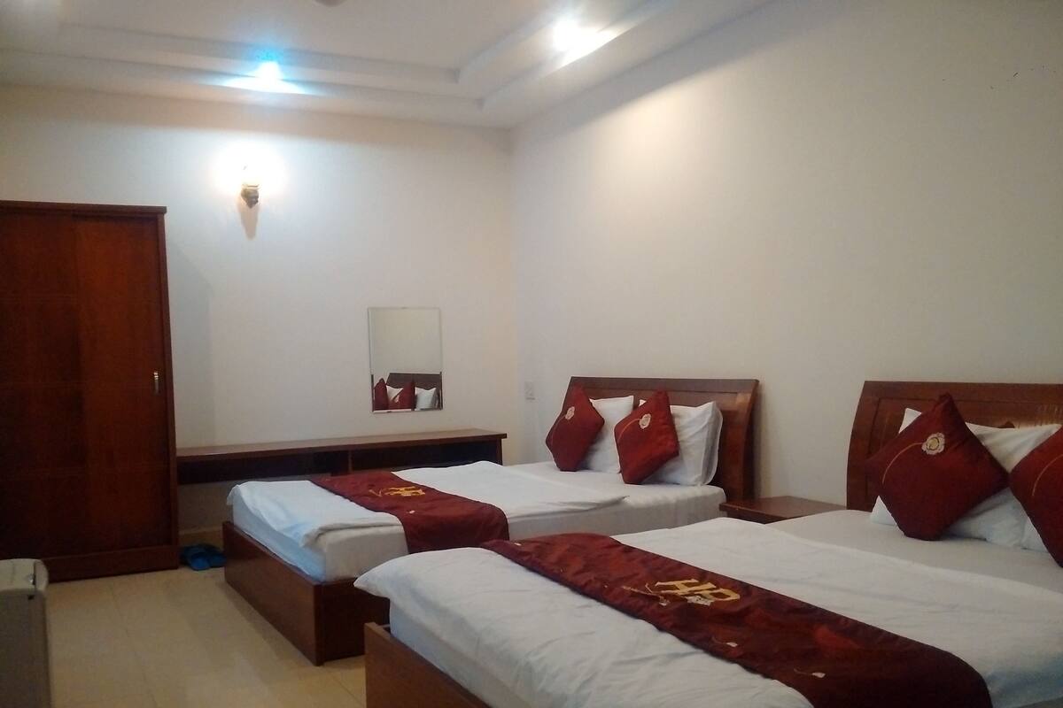 A hotel room with two beds, a wooden wardrobe, a mirror, and a small table.