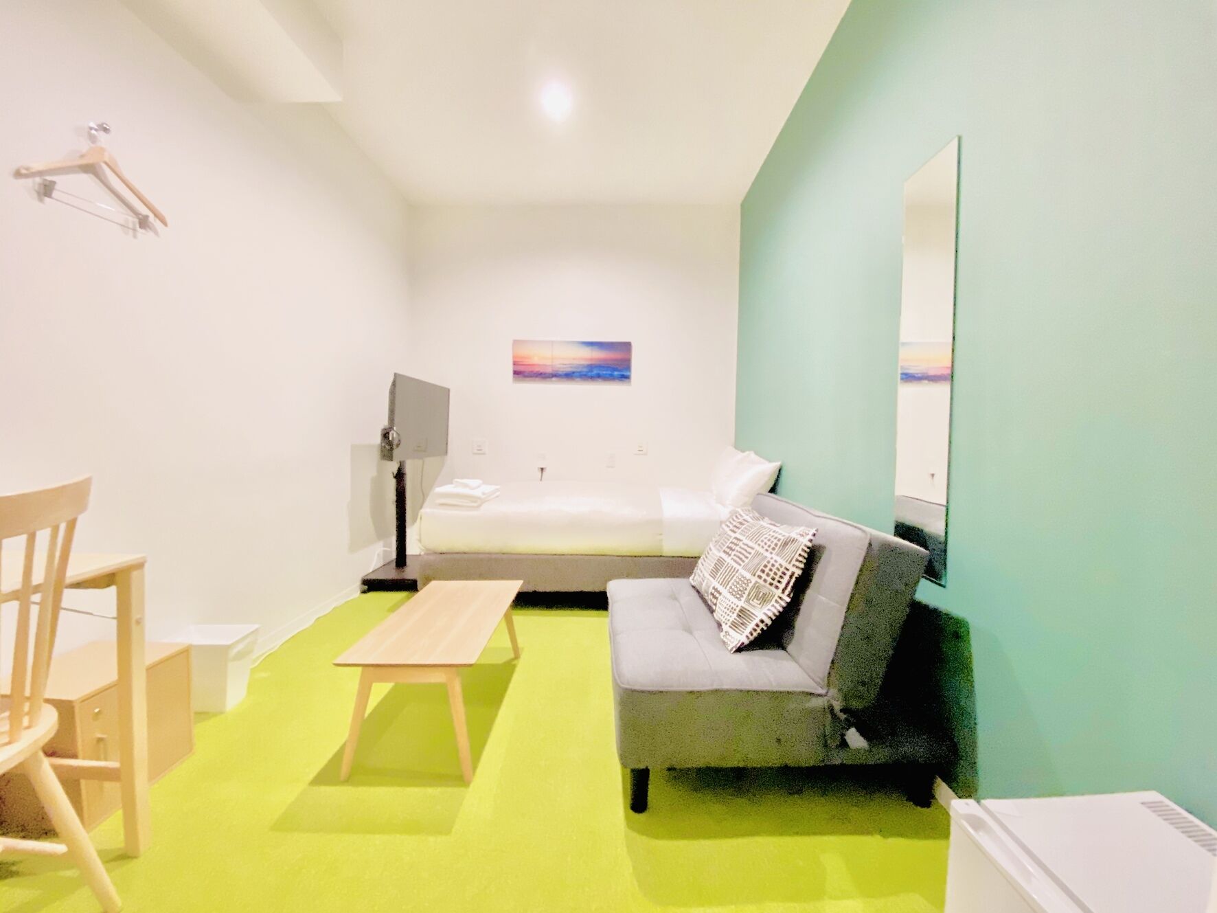 Una habitación con cama, sofá, escritorio, silla, mesa, lámpara y un cuadro en la pared.
