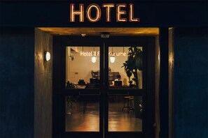 A hotel entrance with a sign reading 'HOTEL' above the doors. Inside, there are tables and chairs, and a person is visible working at a desk. - Hostel ilfaro Kurume (Kurume)
