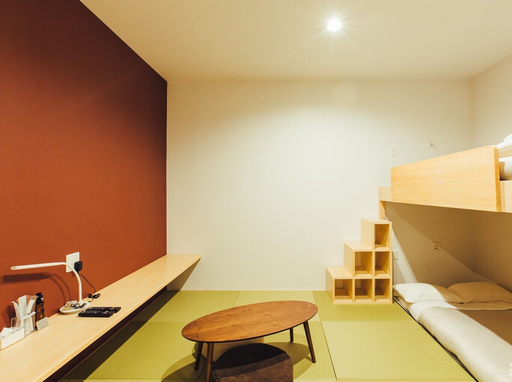 Una habitación minimalista con una cama litera, una pequeña mesa de madera y un escritorio con una lámpara.