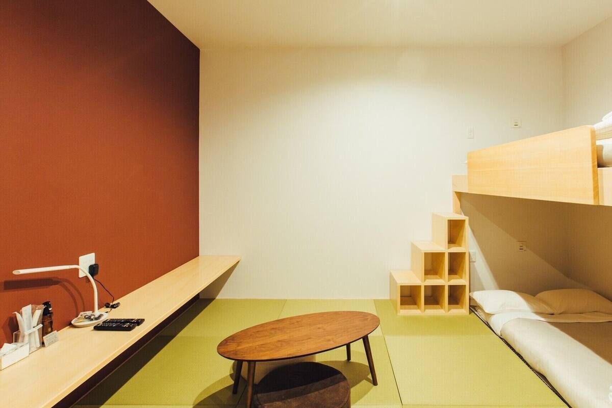 A minimalist room with a bunk bed, a small wooden table, and a desk with a lamp.