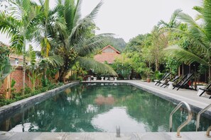 Une piscine rectangulaire, avec un mur en briques d’un côté et une structure en bois en arrière-plan.