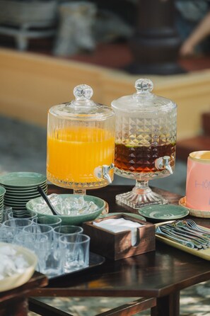Un buffet était dressé avec deux distributeurs en verre, l’un pour le jus d’orange et l’autre pour le thé, le tout entouré d’assiettes et de couverts verts.