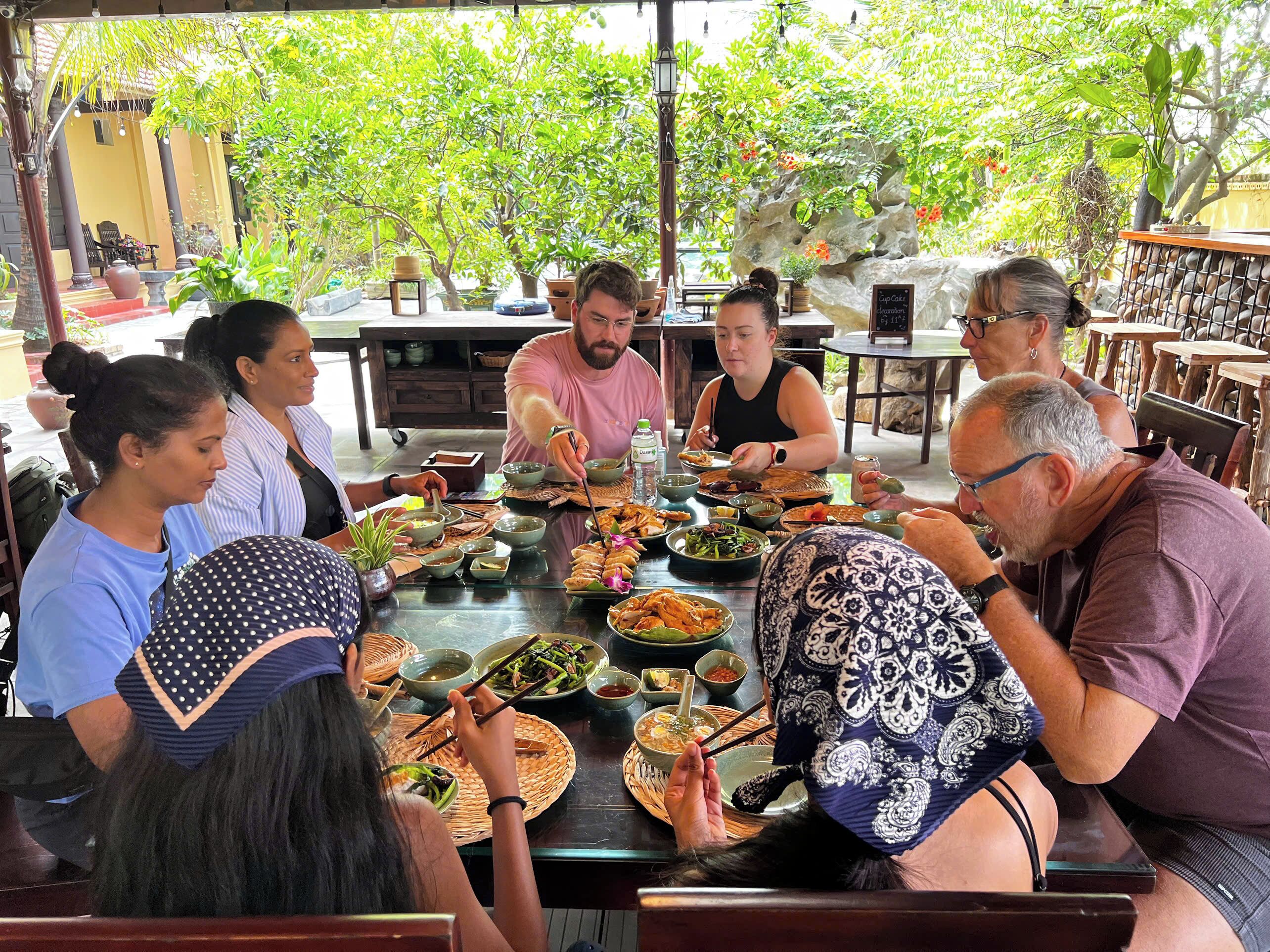 A group of people dining at an outdoor restaurant with a variety of dishes and drinks on the table.