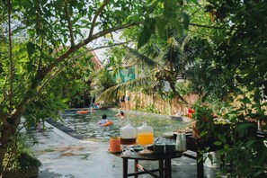 A pool area with people swimming and lounging, surrounded by lush greenery and palm trees. - Amazing Ninh Binh Garden (Hoa Lu)