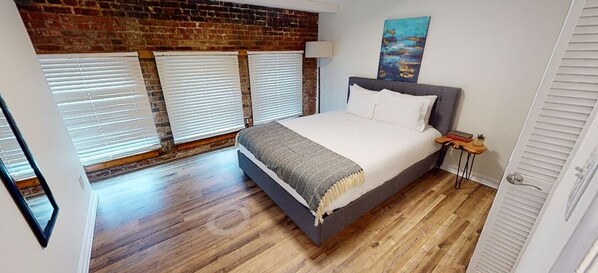 Une chambre à coucher avec un lit, un mur en briques et trois fenêtres équipées de stores.