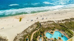Vue aérienne d’un complexe hôtelier en bord de mer, avec une piscine, une plage et l’océan.