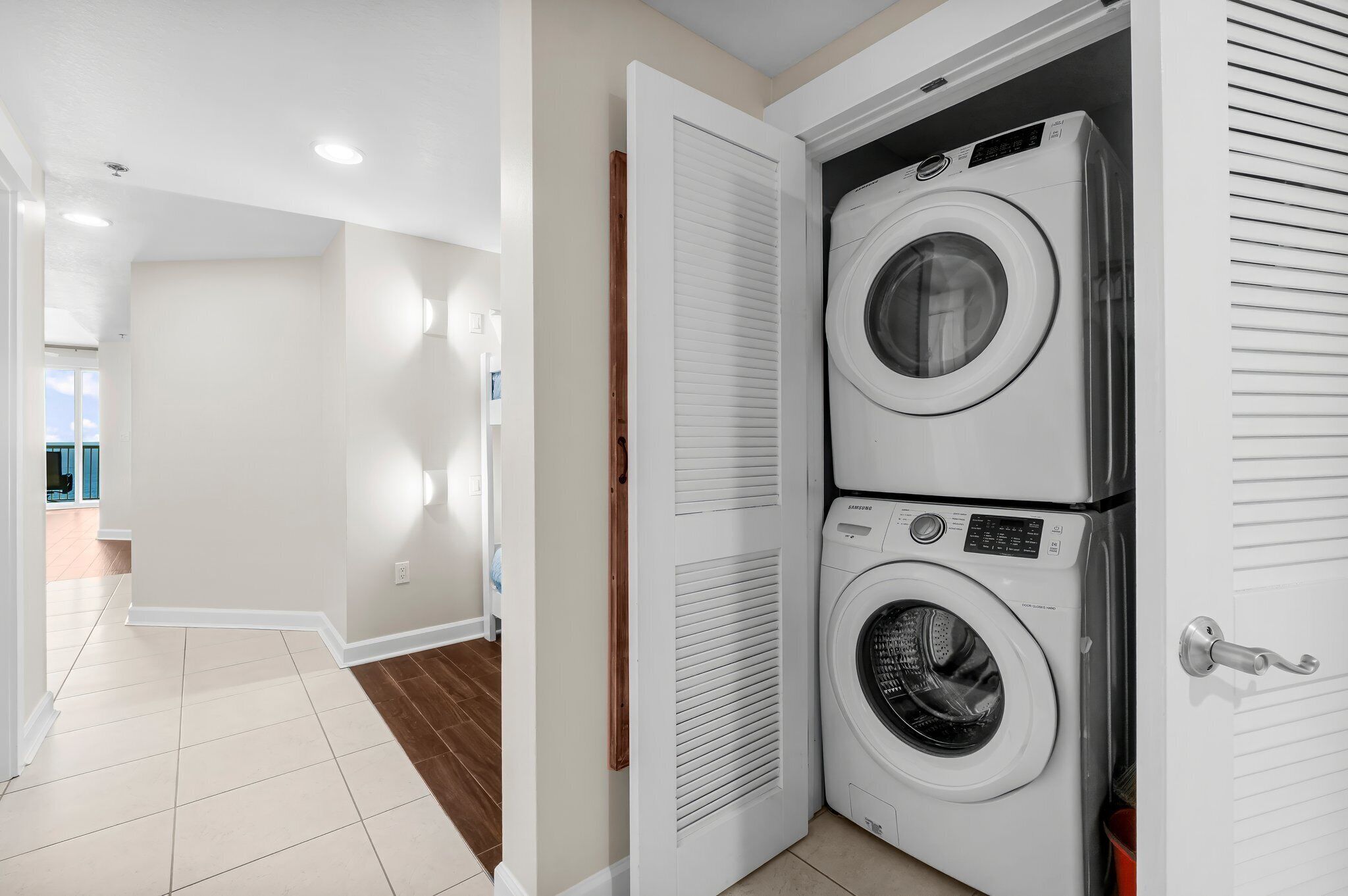 A laundry room with two stacked front-loading washing machines and a door with a handle.