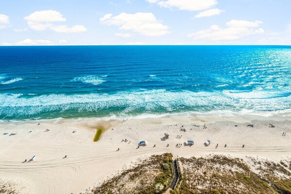 Une plage avec une eau d’un bleu limpide, un rivage sablonneux et quelques parasols.