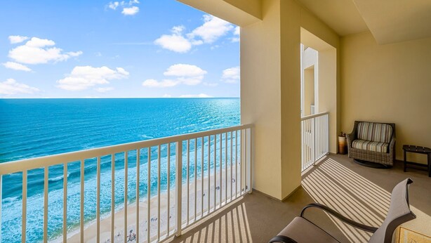 Un balcon avec vue sur l’océan et la plage, une chaise en osier et une petite table.
