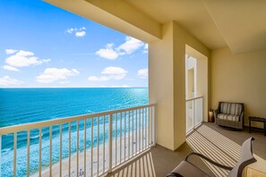 Un balcon avec vue sur l’océan et la plage, une chaise en osier et une petite table.