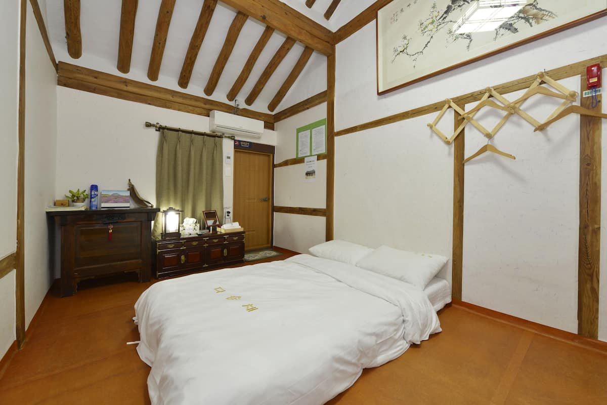 A bedroom with a wooden ceiling, a bed, a dresser, and a hanging rack.