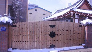 Une porte en bois traditionnelle, de la neige sur le sol, un mur de briques et un bâtiment avec un toit en tuiles.