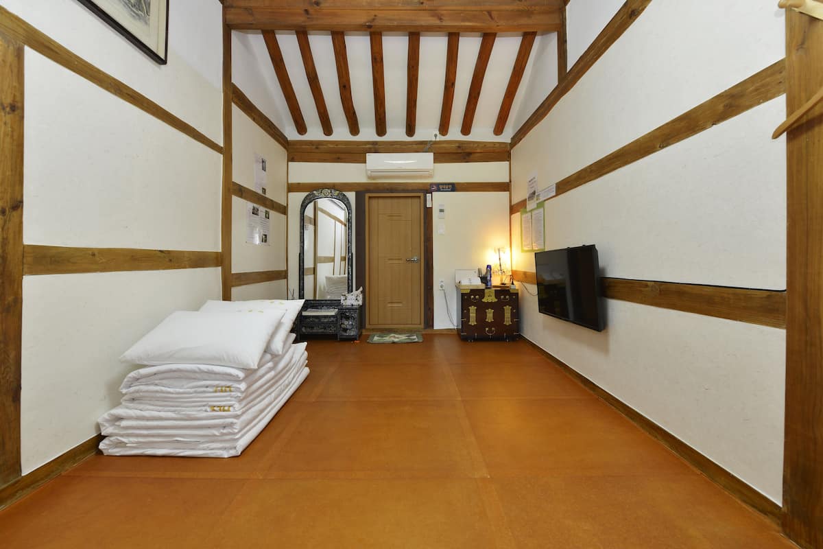 A hallway with a wooden floor, a stack of white towels, a wooden cabinet, a television mounted on the wall, and a door at the end.