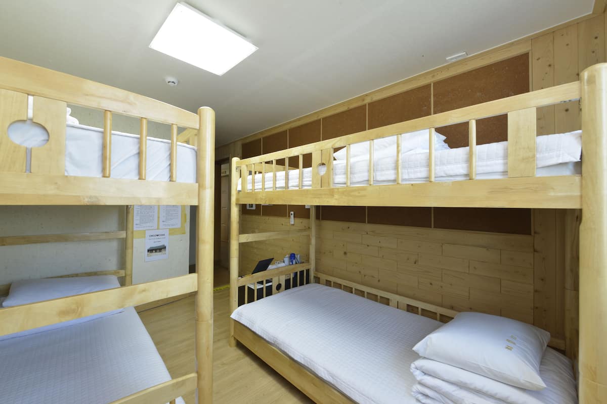 A bunk bed room with wooden walls, a ceiling light, and a small table with a chair.