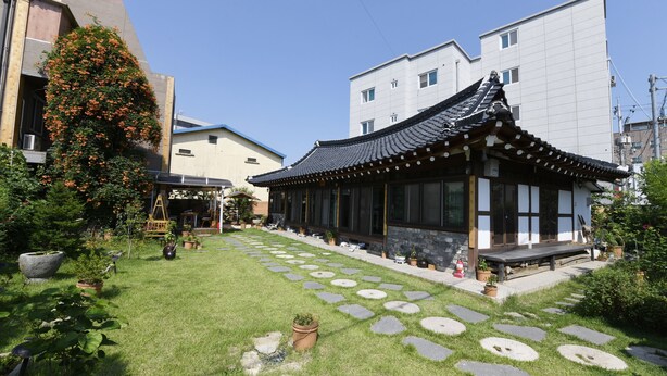 Un bâtiment traditionnel japonais, doté d’un toit recouvert de tuiles et d’un chemin de pierre menant à un banc en bois.