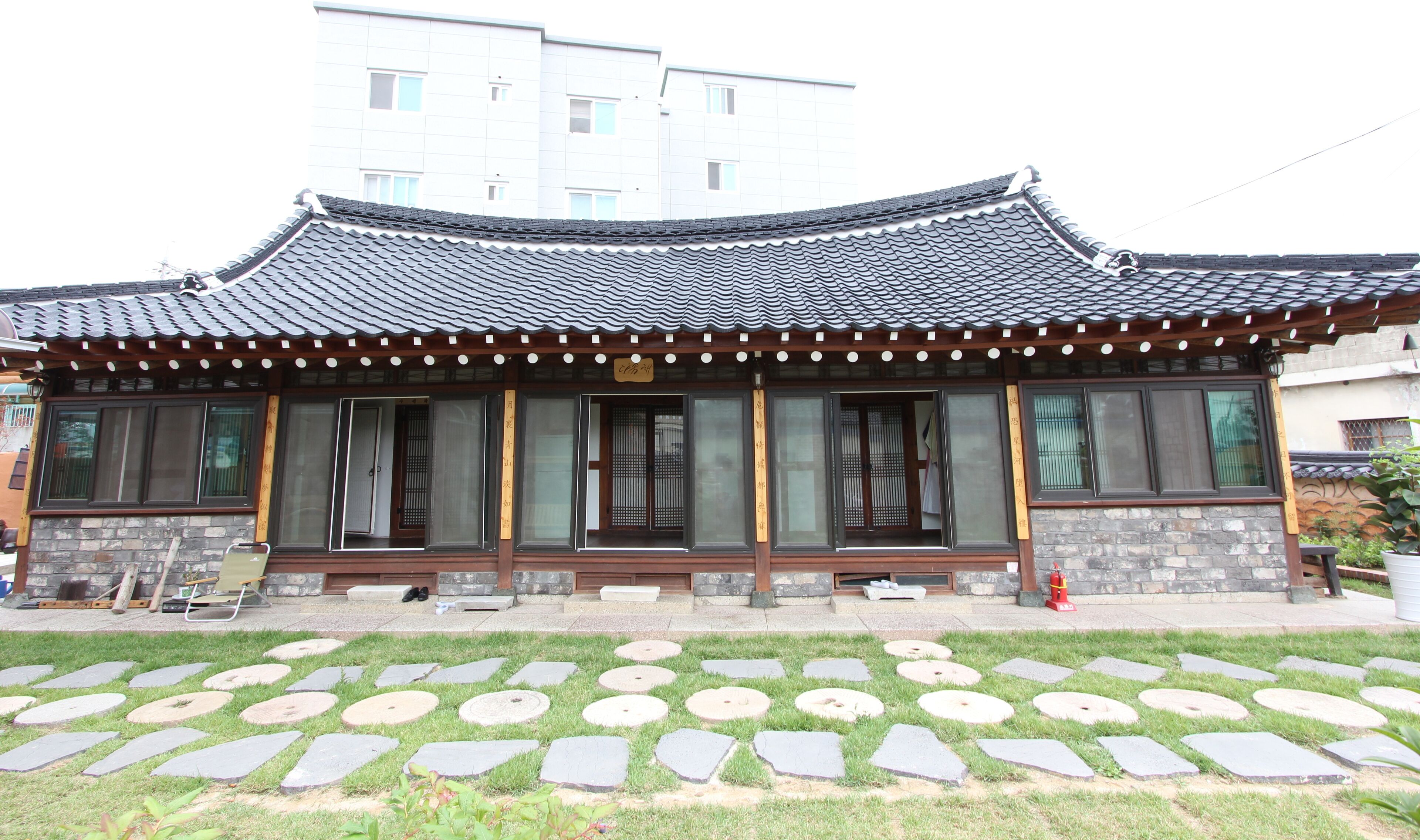 A traditional Korean-style building with a tiled roof, large windows, and a stone pathway in front.