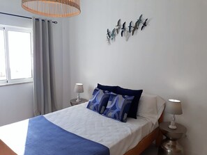 Een slaapkamer met een bed, twee bedlampen, een raam met gordijnen en een decoratie van vogels aan de muur.