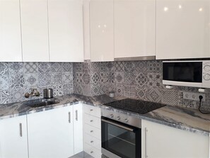 Een moderne keuken met witte kasten, een zwart fornuis, een magnetron en betegelde spatwand.