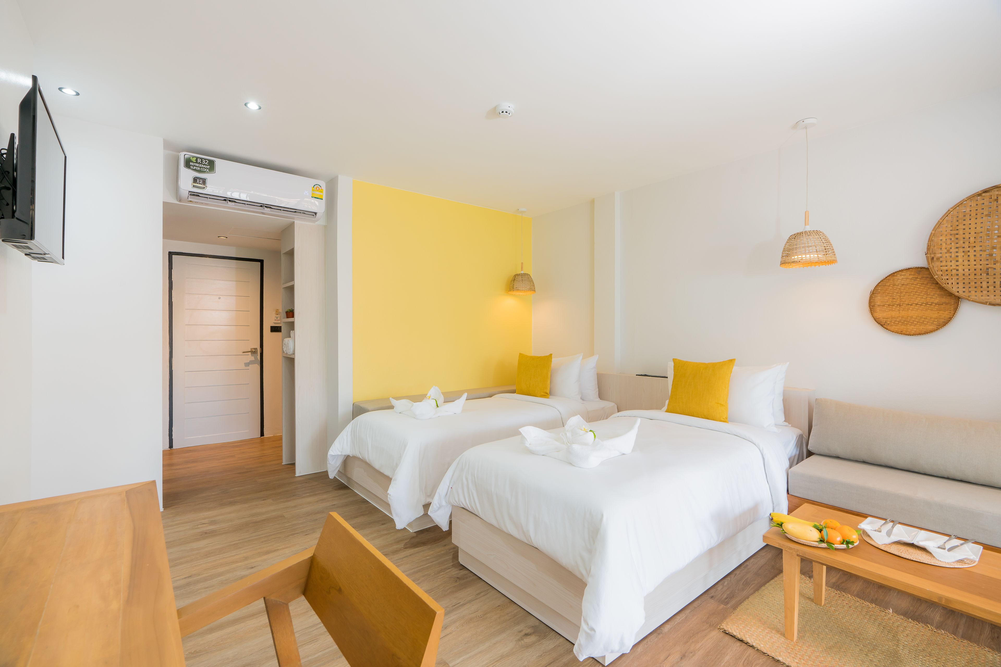 A hotel room with two beds, a sofa, a wooden table, and a wall-mounted air conditioner.