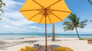 A beach with two lounge chairs under a large yellow umbrella, a palm tree, and a view of the ocean. - Princess Paradise Koh Phangan (Ko Pha-ngan)