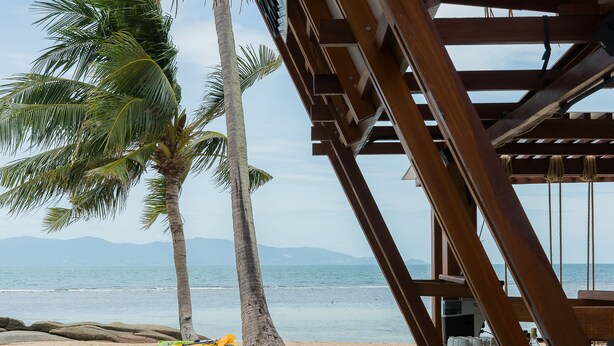 A pool with clear water, surrounded by wooden structures and palm trees, overlooking a beach and ocean. - Princess Paradise Koh Phangan (Ko Pha-ngan)