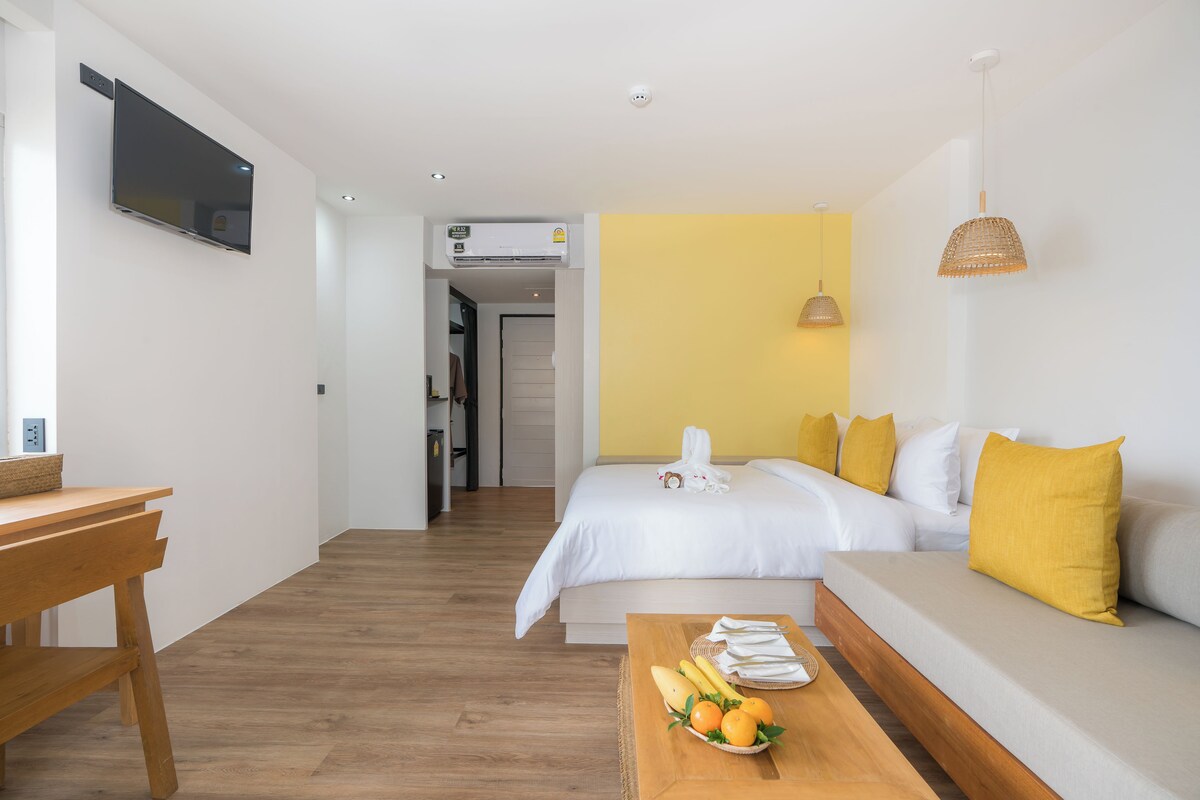 Une chambre d’hôtel moderne équipée d’un lit, d’un canapé, d’une table en bois avec des fruits, d’une télévision et d’un climatiseur.