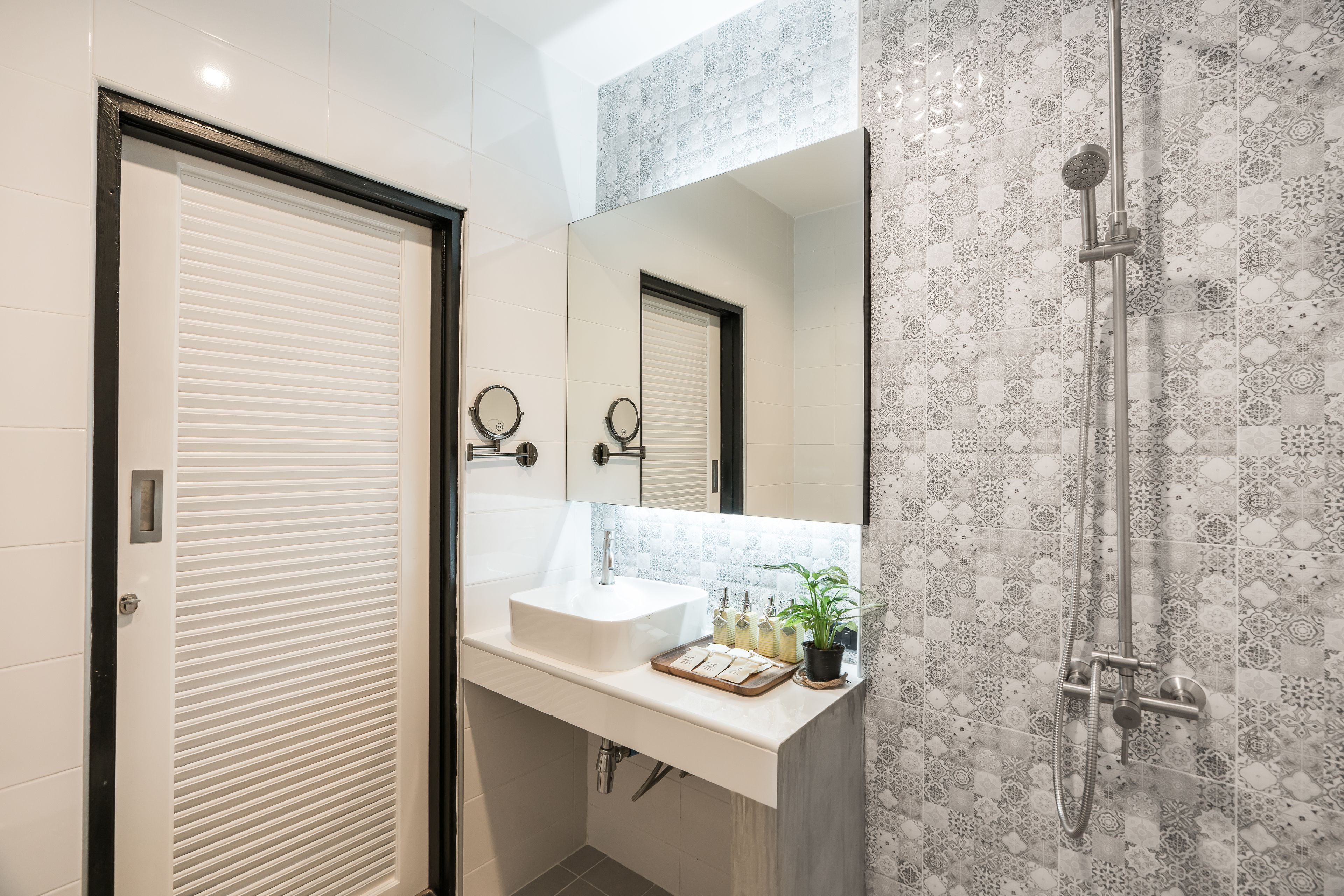 A bathroom with a white sink, a mirror, a shower, and patterned tiles.