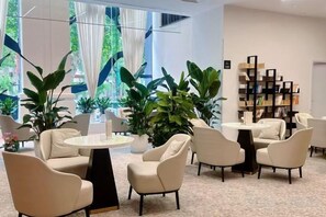 Ein stilvoller Lounge-Bereich mit runden Tischen und Stühlen, einem Bücherregal und großen Fenstern mit Vorhängen.