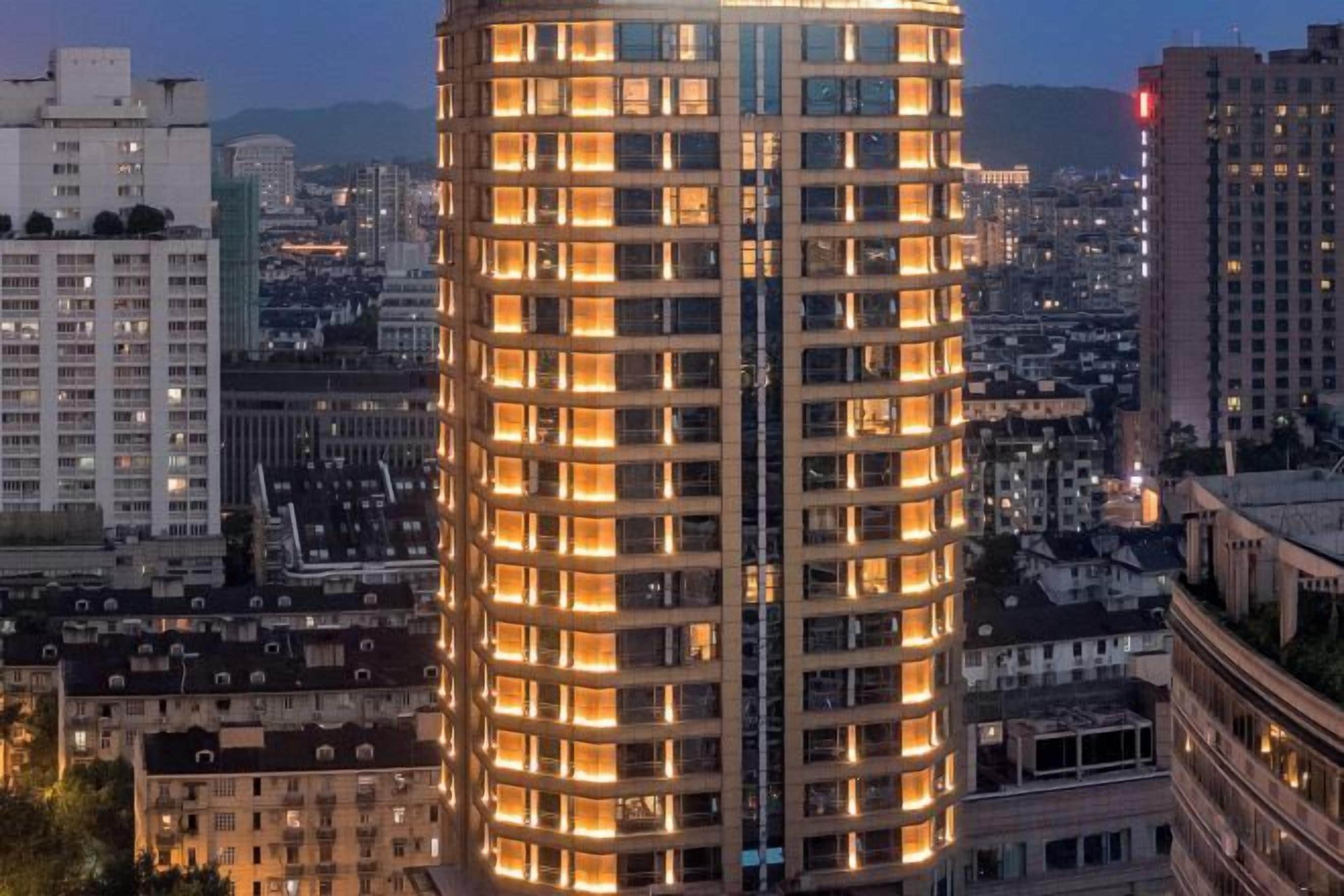 A tall, cylindrical hotel with multiple floors and illuminated windows, surrounded by other buildings.
