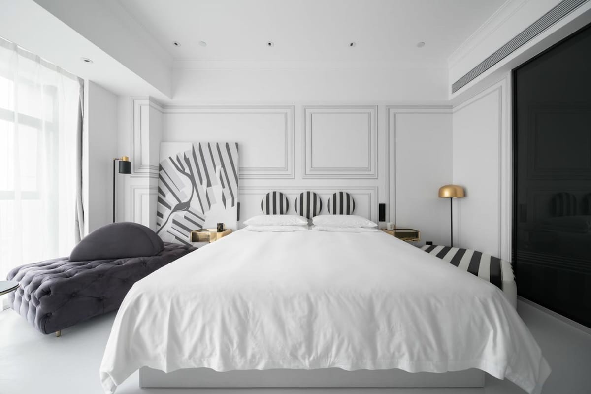 Un dormitorio moderno con una cama grande, un banco tapizado de color gris y un cuadro abstracto de gran tamaño en la pared.