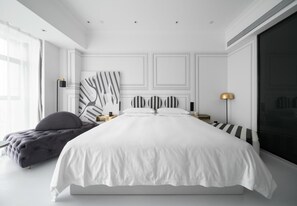 Un dormitorio moderno con una cama grande, un banco tapizado de color gris y un cuadro abstracto de gran tamaño en la pared.
