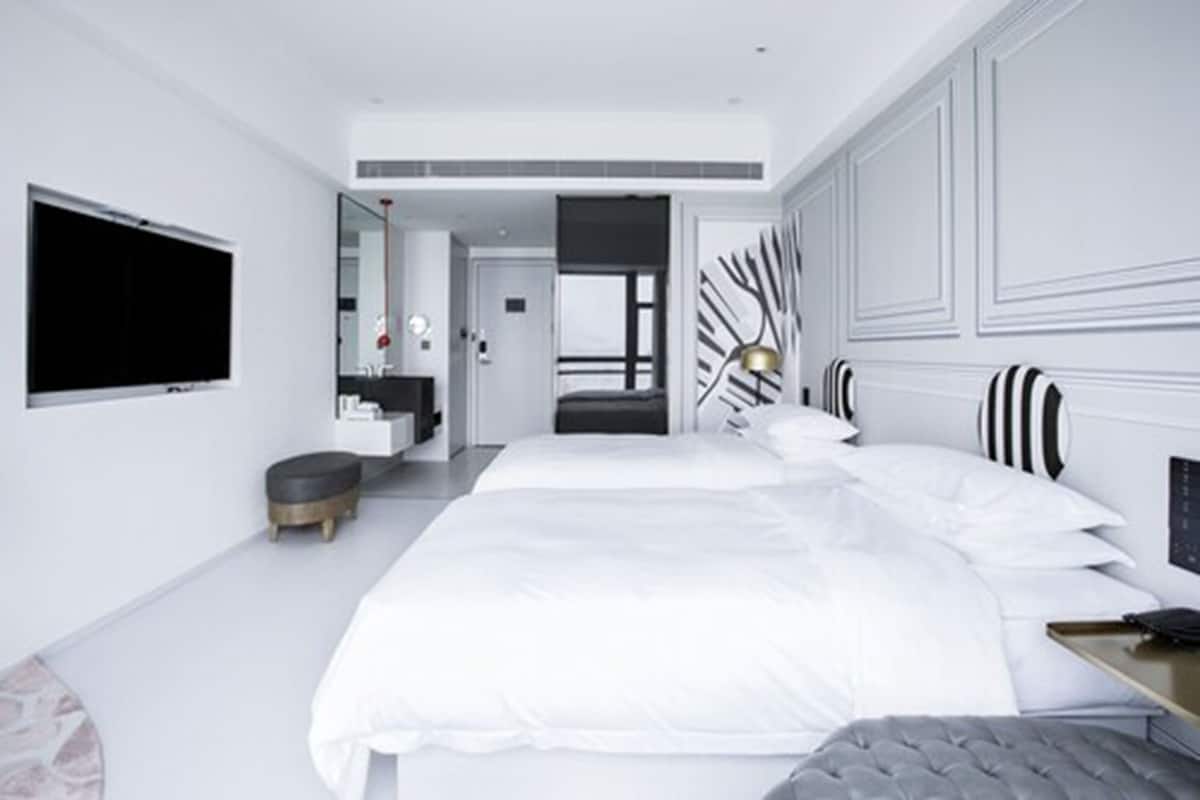 Una habitación de hotel moderna con una cama grande, una mesita de noche, un televisor y un espejo.