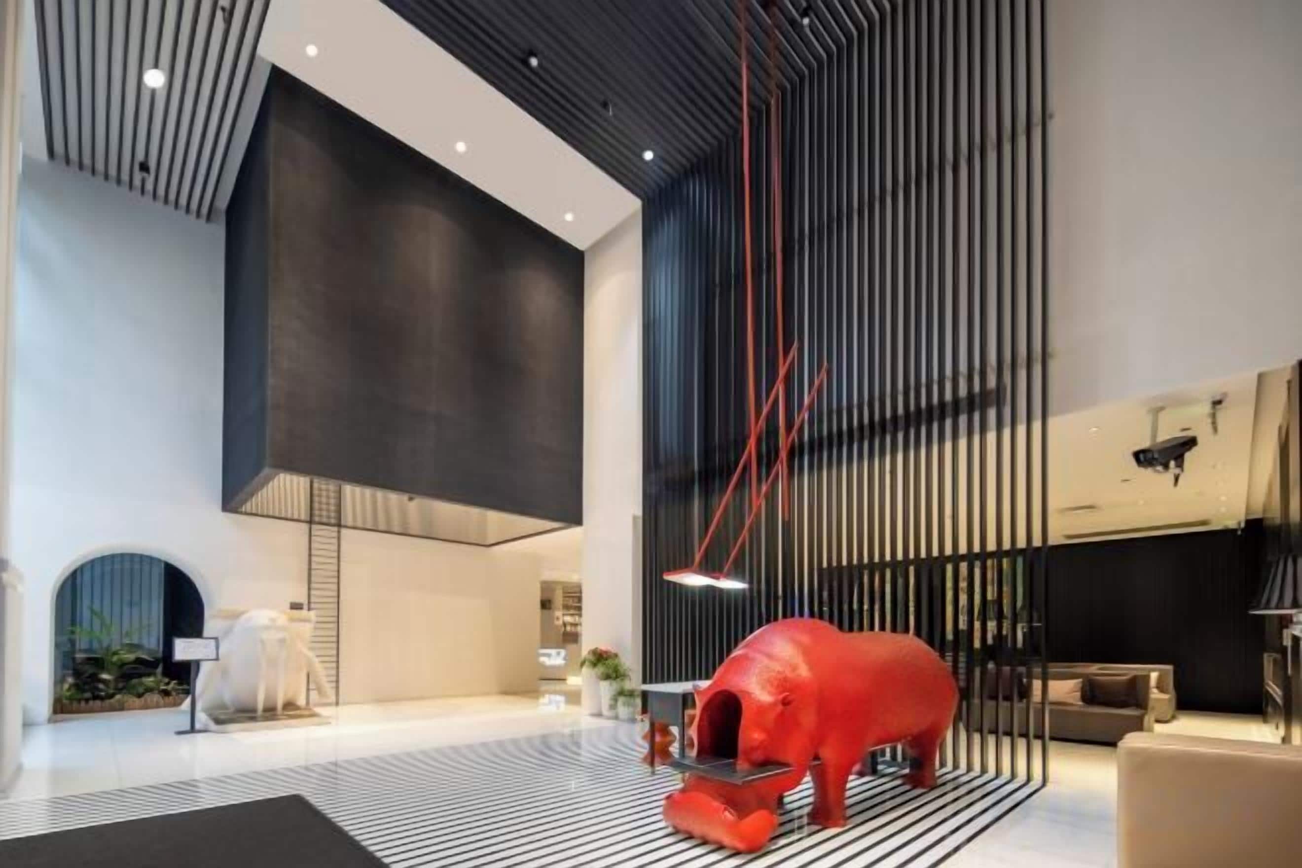 Un hall d’entrée spacieux au design moderne, agrémenté d’une grande sculpture rouge, d’un sol à rayures noires et blanches et d’un plafond haut orné de lignes verticales.