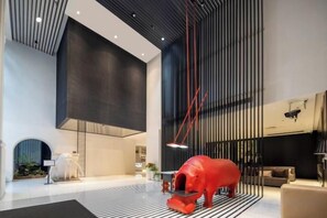 Un hall d’entrée spacieux au design moderne, agrémenté d’une grande sculpture rouge, d  ’un sol à rayures noires et blanches et d’un plafond haut orné de lignes verticales.