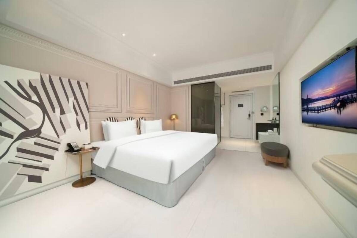 Habitación de hotel moderna con una cama grande, una mesita de noche, una silla, un espejo y un cuadro en la pared.