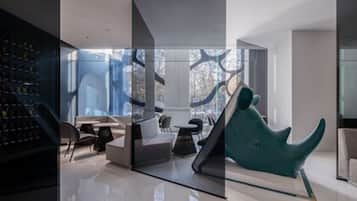 A modern interior with a glass partition, a collection of shoes on the left, a teal chair, and a sofa.