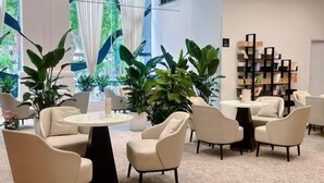 Un interior moderno con mesas redondas y sillas color beige, ventanas amplias con cortinas y una estantería.