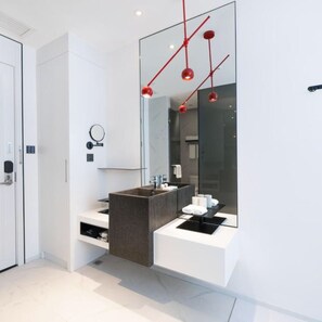 Un baño moderno con un espejo grande, un tocador oscuro y lámparas colgantes rojas.