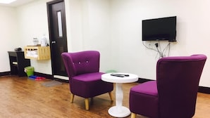 A room with two purple chairs, a small white table, and a television mounted on the wall. - Lotus B&B (Hualien City)