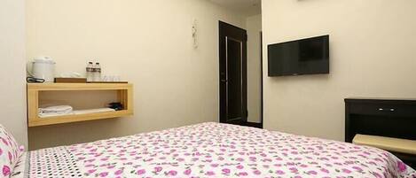 A bedroom with a bed, a TV, an air conditioner, and a shelf with toiletries.