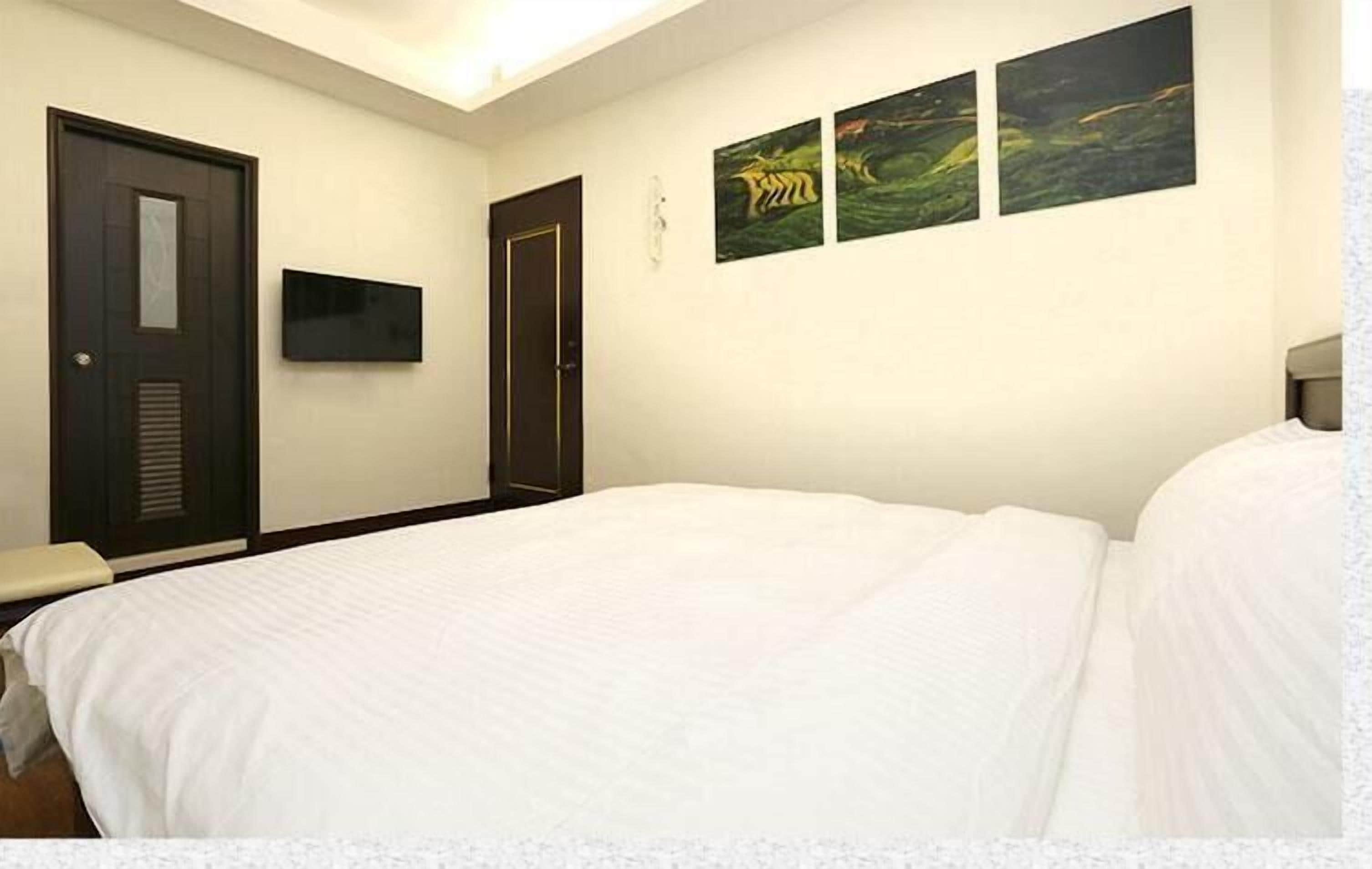 A hotel room with a large bed, two doors, a flat-screen TV, and three landscape paintings on the wall.