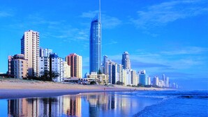 A coastal cityscape with high-rise buildings, a beach, and calm waters reflecting the skyline. - The Towers Chevron Renaissance Holidays Gold Coast (Surfers Paradise)