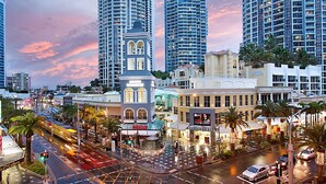 A cityscape with modern high-rise buildings, a historic building with arched windows, and a busy street with palm trees. - The Towers Chevron Renaissance Holidays Gold Coast (Surfers Paradise)